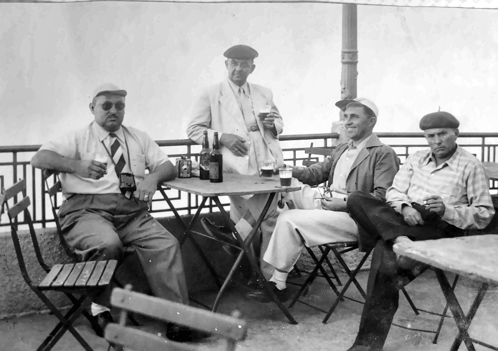 Quatro homens de boina e chapéu em mesa de café, fotografia em preto e branco