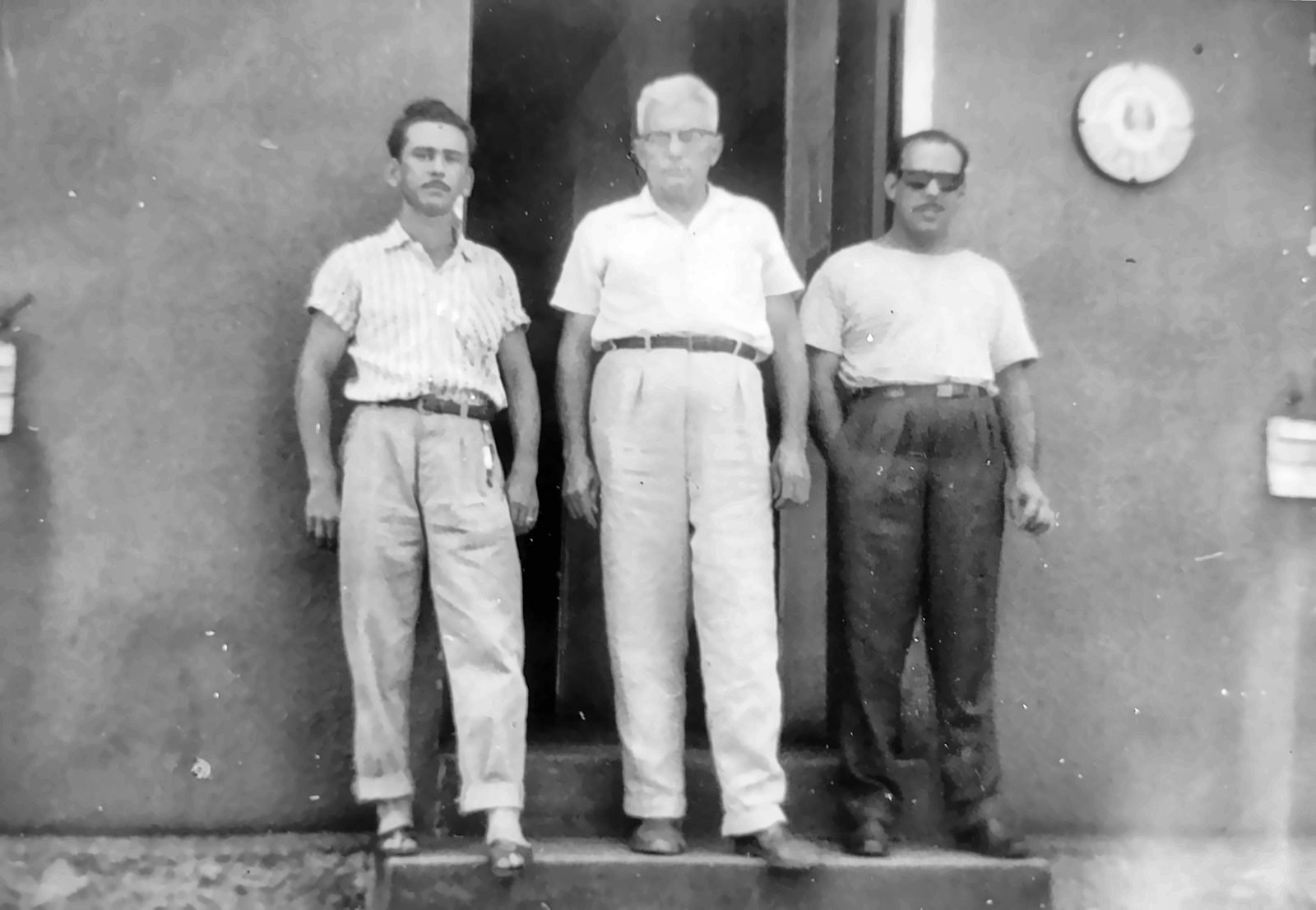 Três homens na porta de um prédio, fotografia em preto e branco